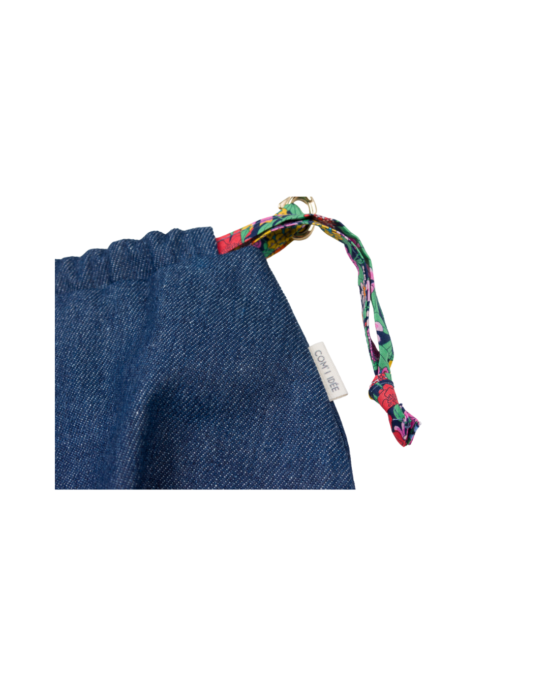 Gros plan sur le lien coulissant en tissu Liberty fleuri et l’étiquette COM'1 IDÉE du sac bourse Alix en denim bleu