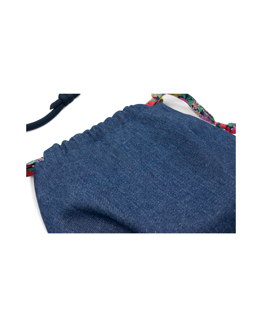 Gros plan sur le tissu denim bleu du sac bourse Alix avec finition froncée et détails en tissu Liberty fleuri multicolore.