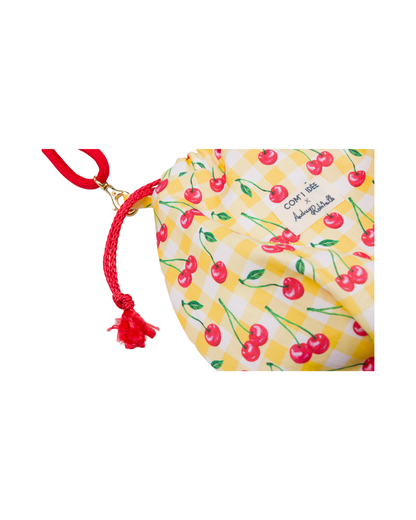 Gros plan sur le tissu imprimé cerises, le cordon de serrage rouge et l’étiquette COM'1 IDÉE x Audrey Robitaille du sac bourse Telma.